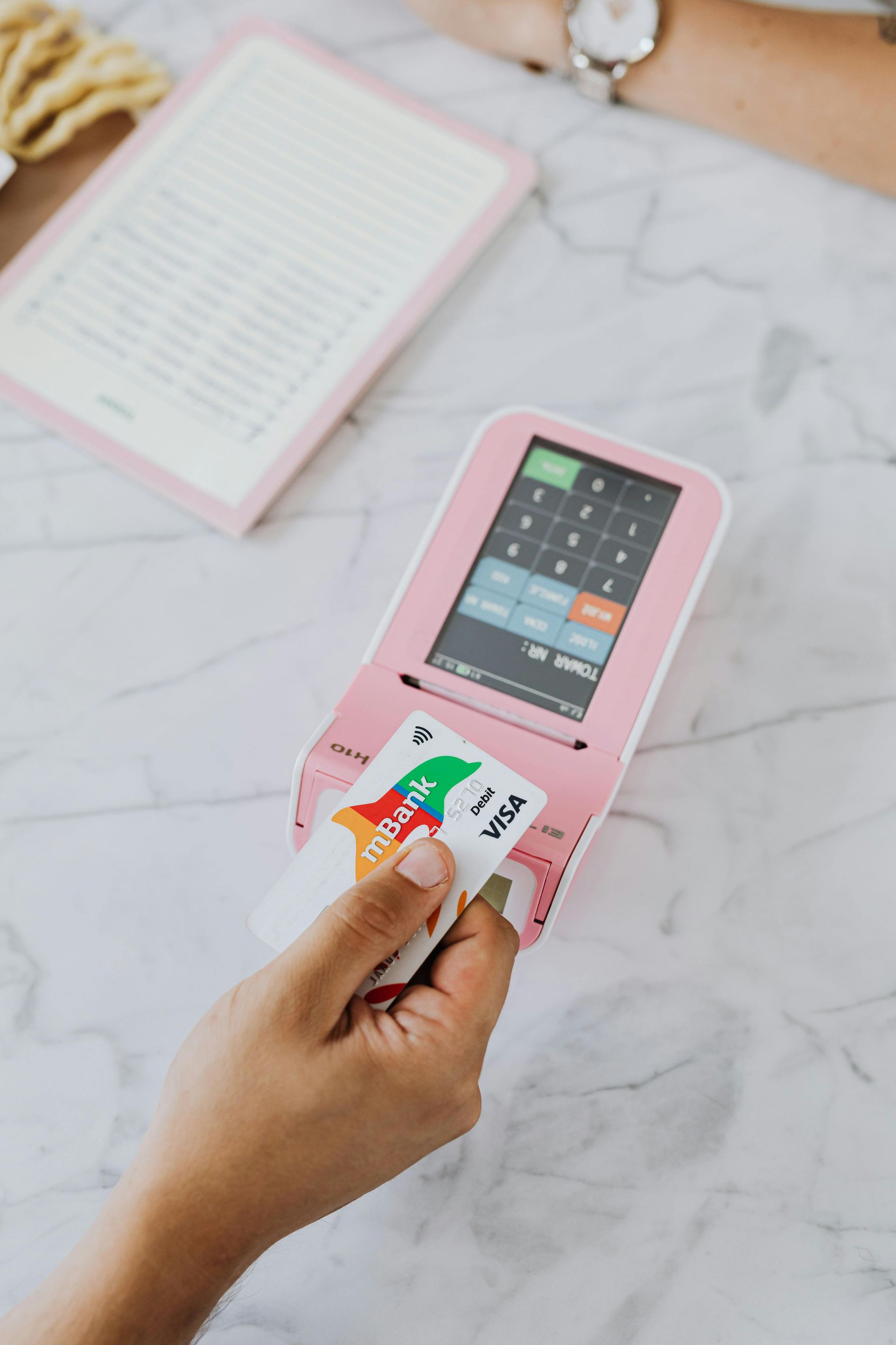 Een hand houdt een visa card bij een betaalautomaat.