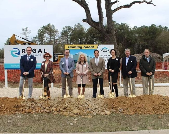 Group of people at a groundbreaking ceremony, holding shovels, with construction signs and equipment in the background.