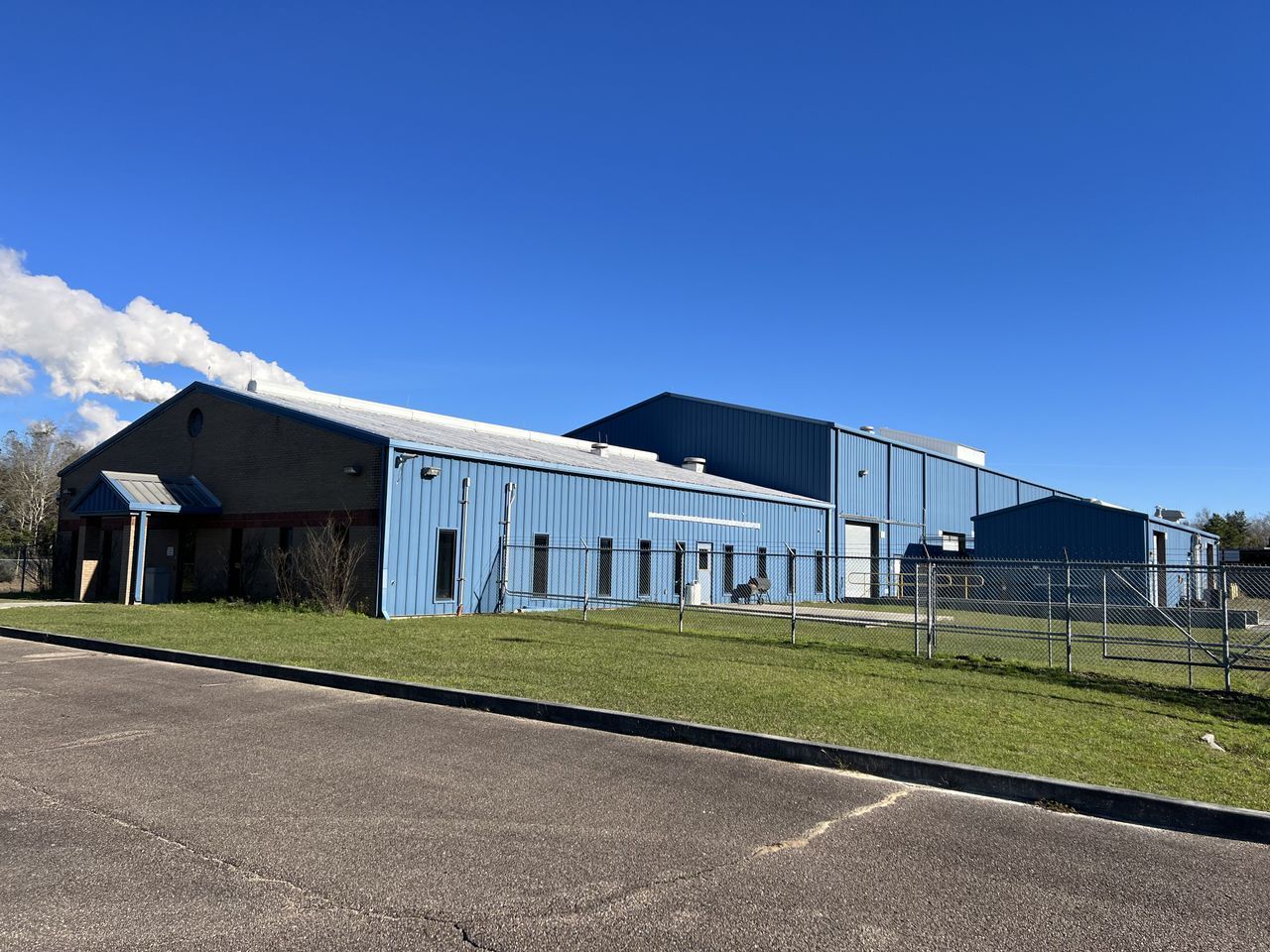Blue metal building with chain-link fence and green lawn against a bright blue sky.