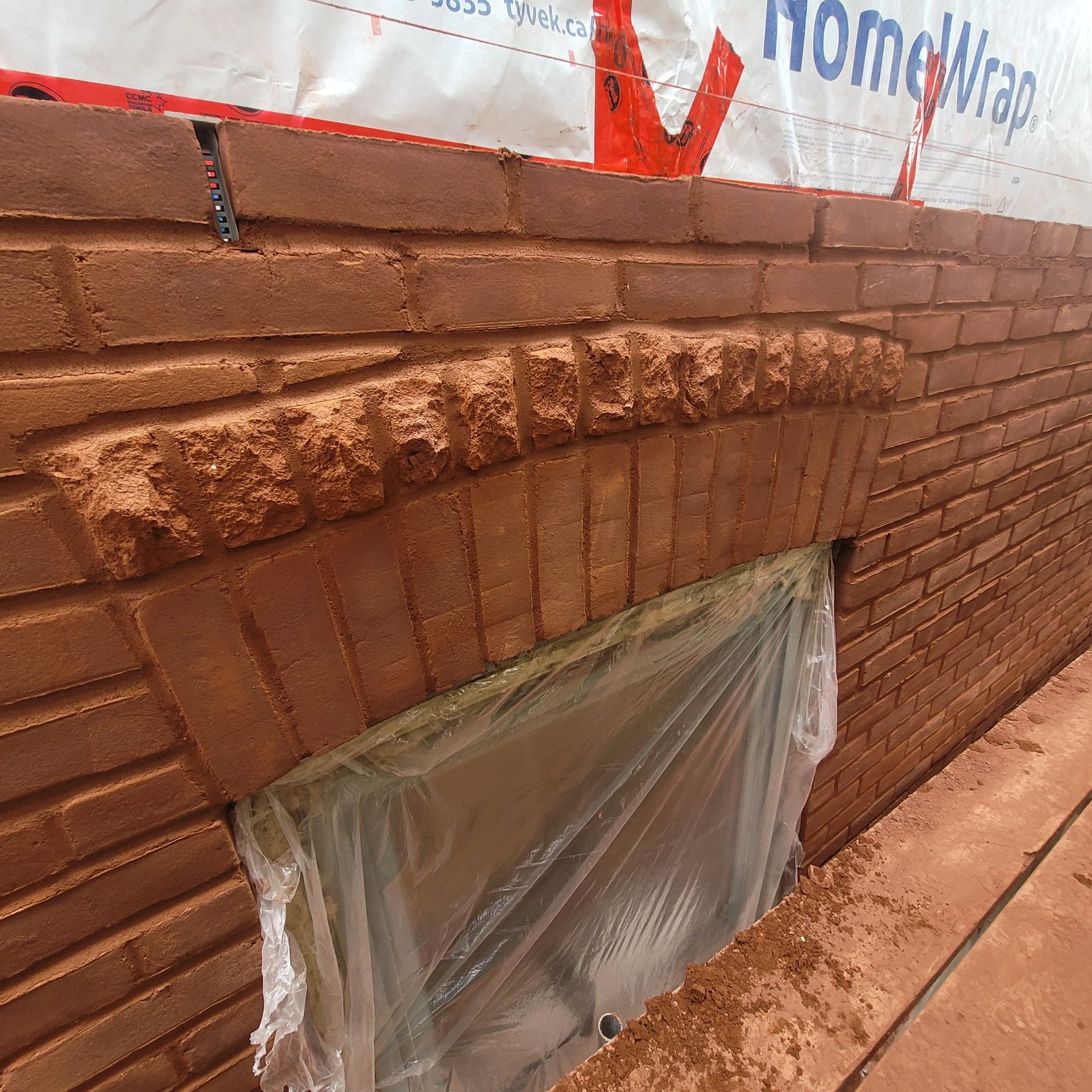 Un mur de briques avec une fenêtre recouverte de plastique et un panneau indiquant homewrap