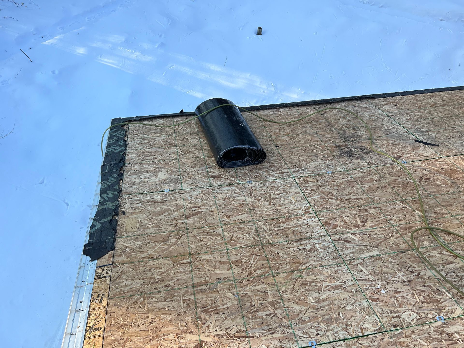 A roll of black roofing underlayment rests on a wooden roof deck after ice dam removal in Gaylord, MI.