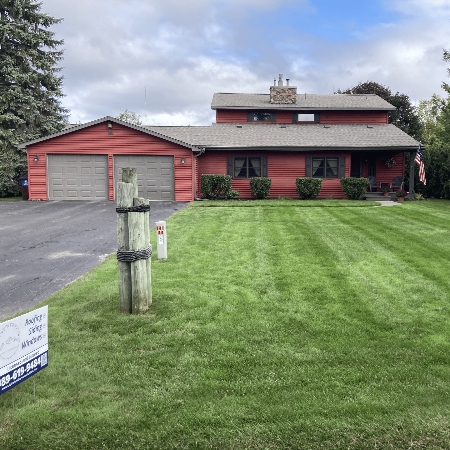 House with red siding, two light grey garage doors and a new asphalt shingle roof installation