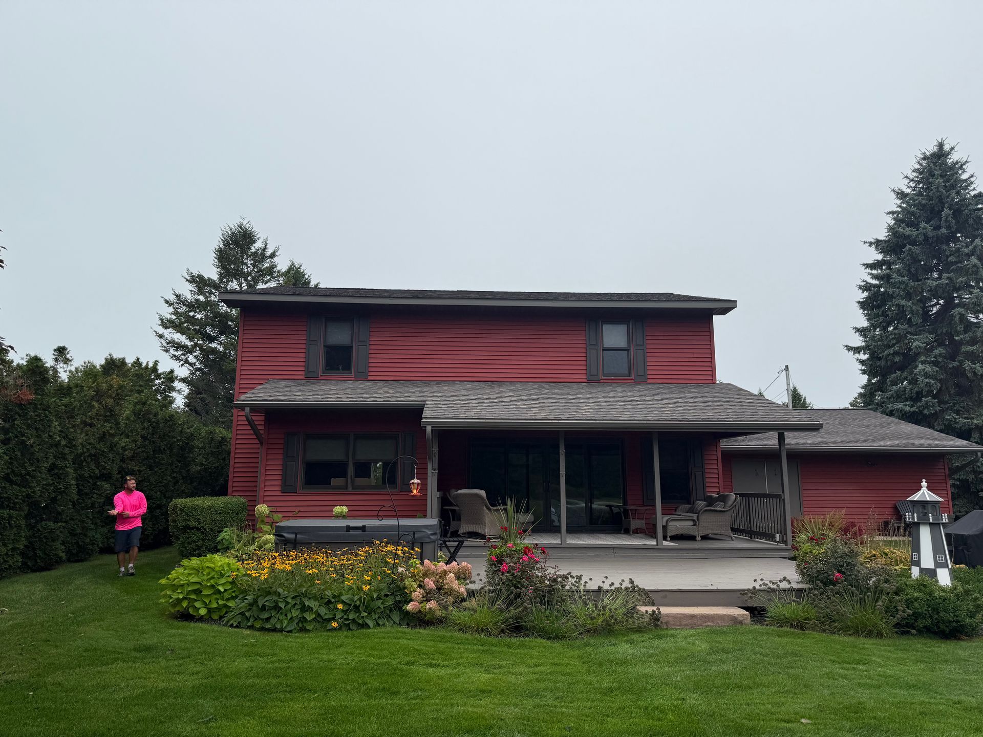 House featuring red vinyl siding and a new asphalt roof, with an Alpine Brothers Construction member walking to the left.