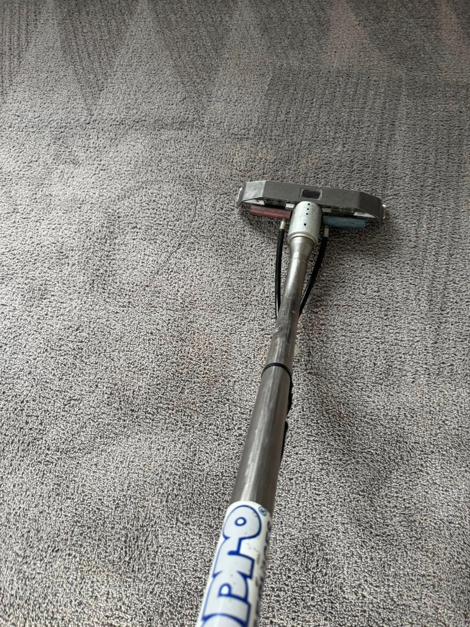 Carpet cleaning tool in use on a gray carpet, removing dirt.
