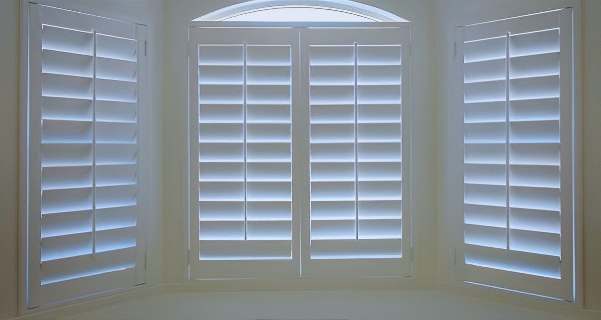 A room with three white shutters on a window.