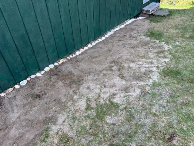 A dirt path leading to a green fence in a backyard.