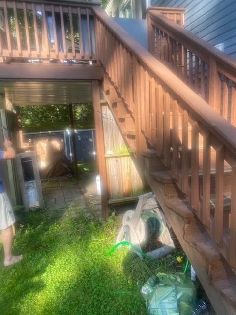 A wooden deck with stairs leading up to it and a hose in the grass.