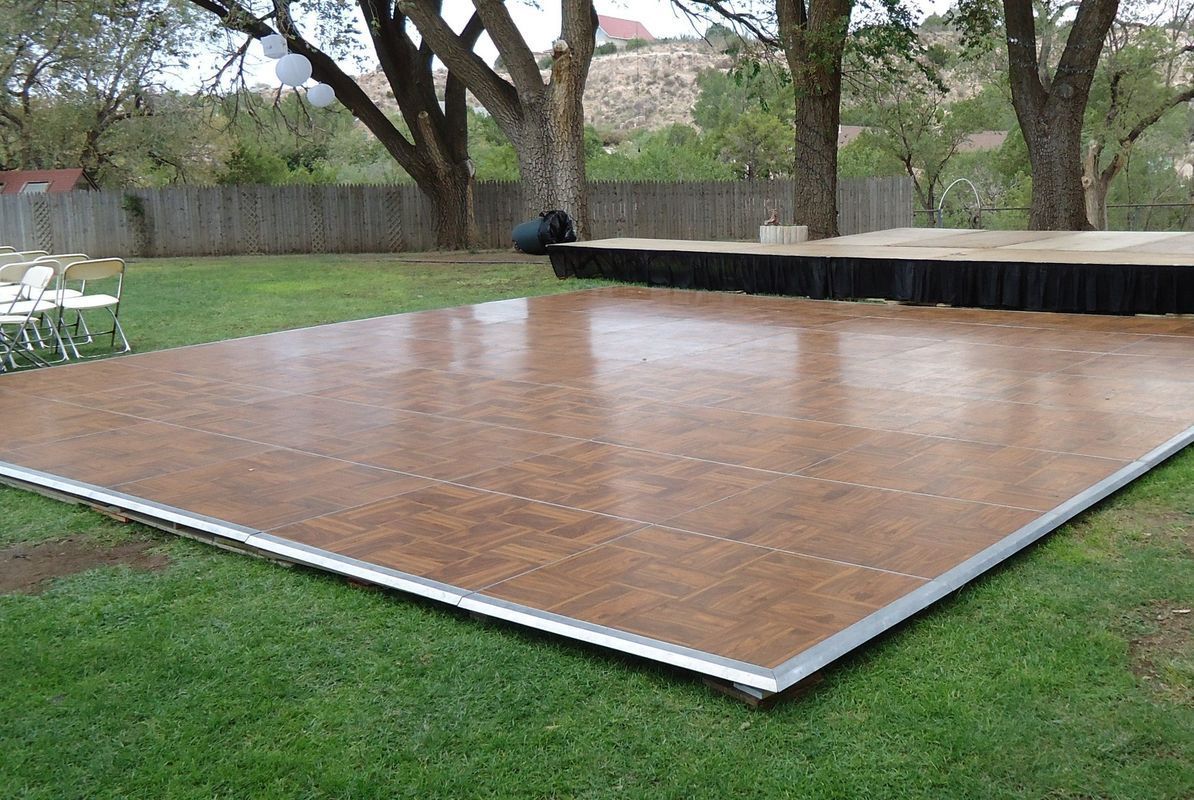A large wooden dance floor is sitting on top of a lush green field
