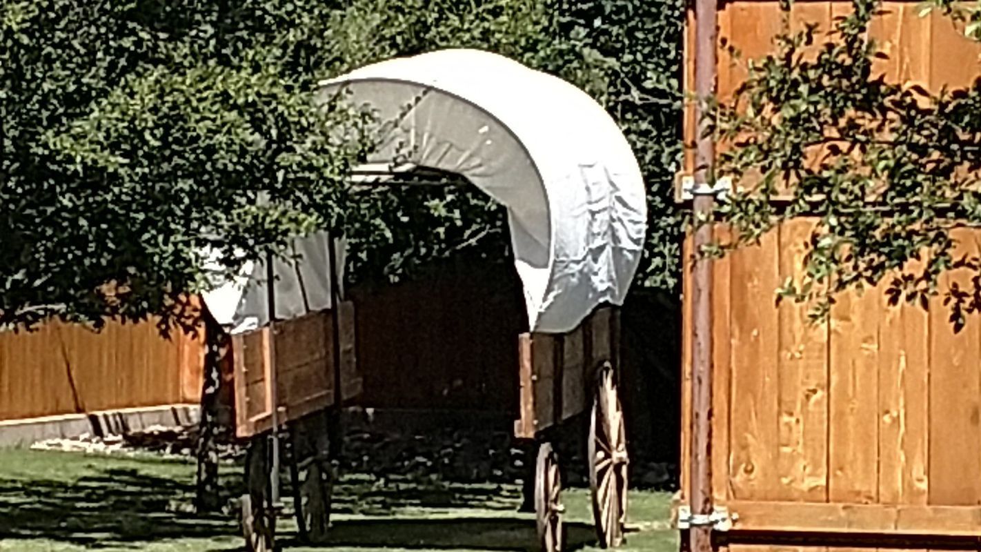A covered wagon is parked in front of a wooden fence
