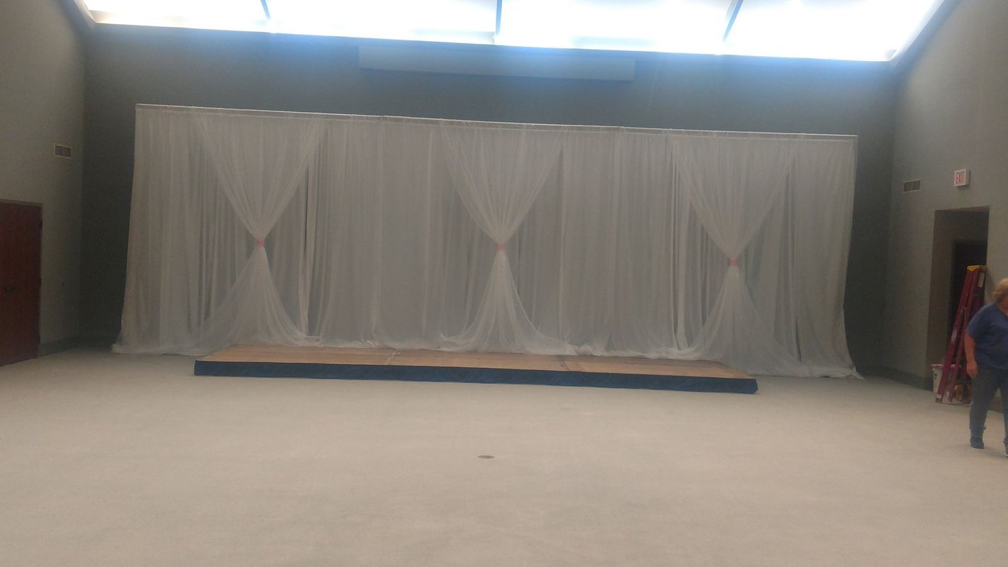 A large empty room with a stage and white curtains