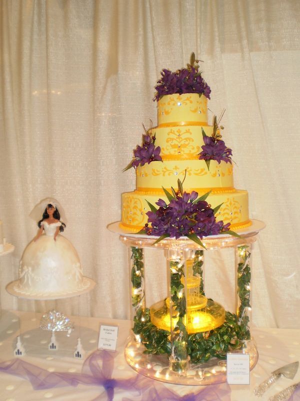 A yellow wedding cake with purple flowers and a bride and groom cake topper
