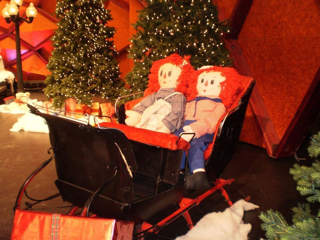 Two dolls in a sleigh with christmas trees in the background