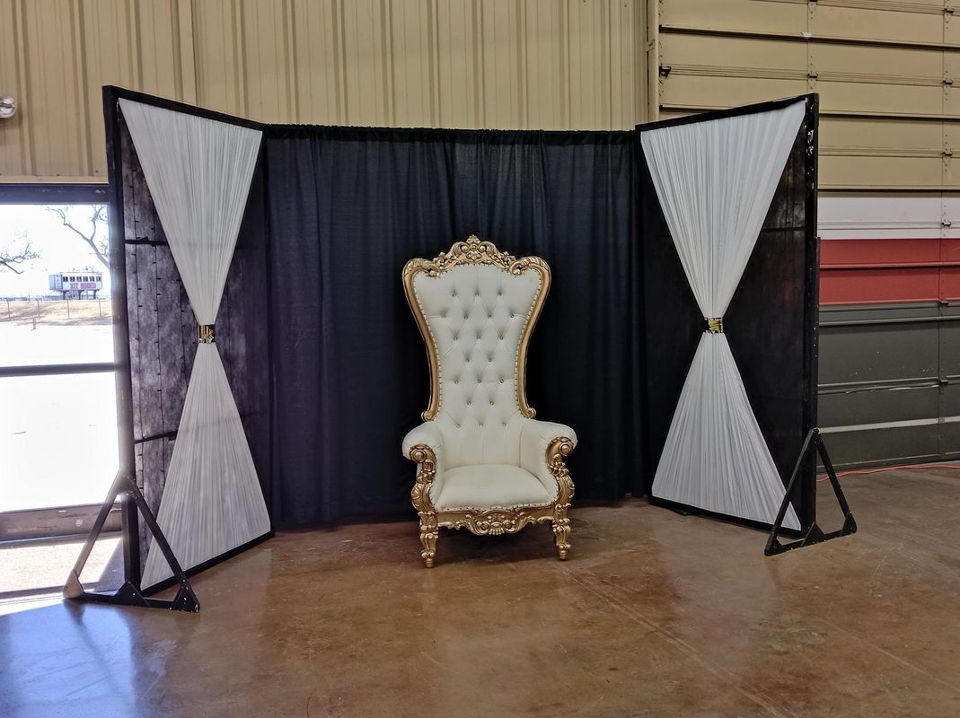 A white and gold chair is sitting in front of a black curtain