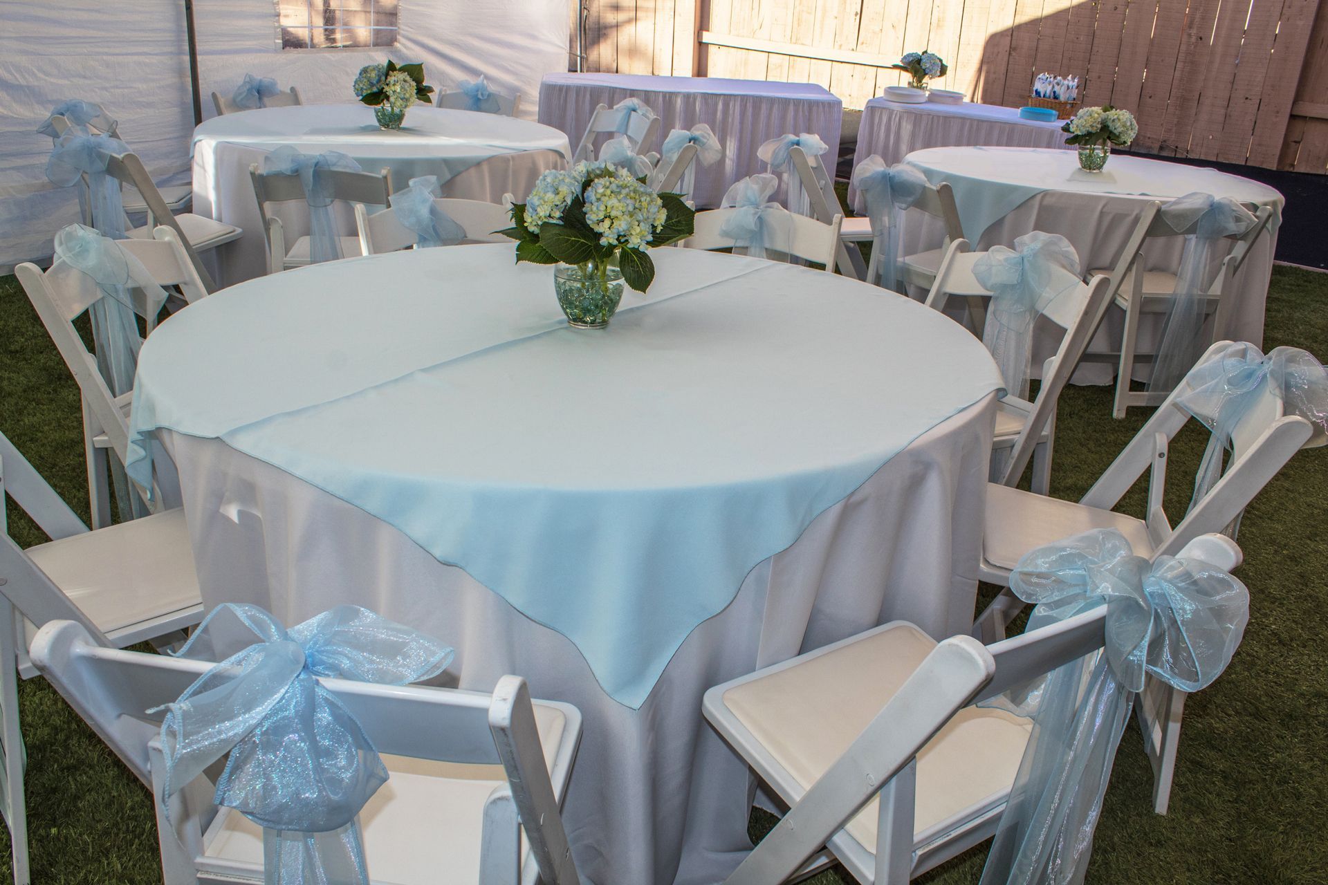A table with a blue table cloth and white chairs