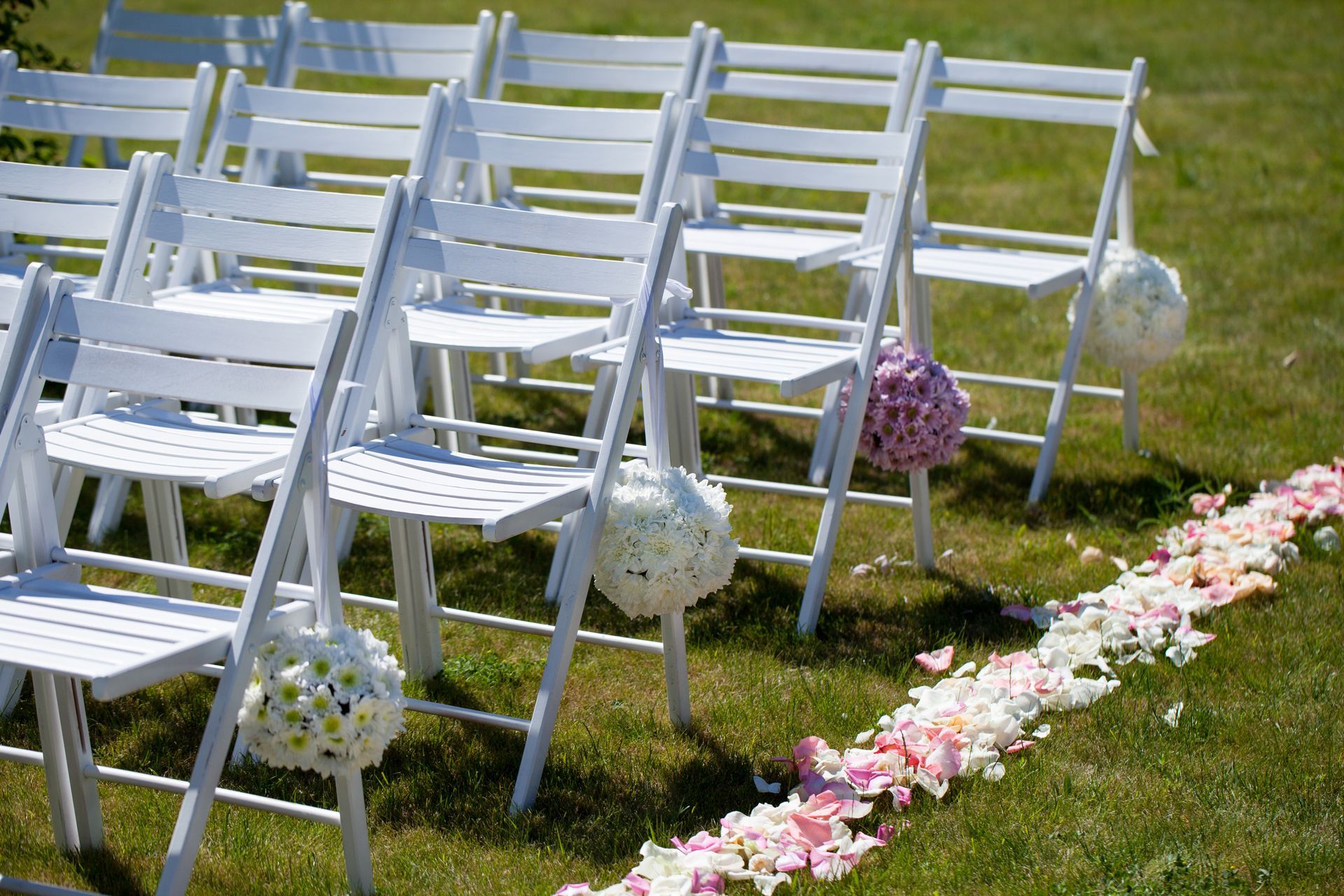 A row of white folding chairs are lined up in a grassy field.
