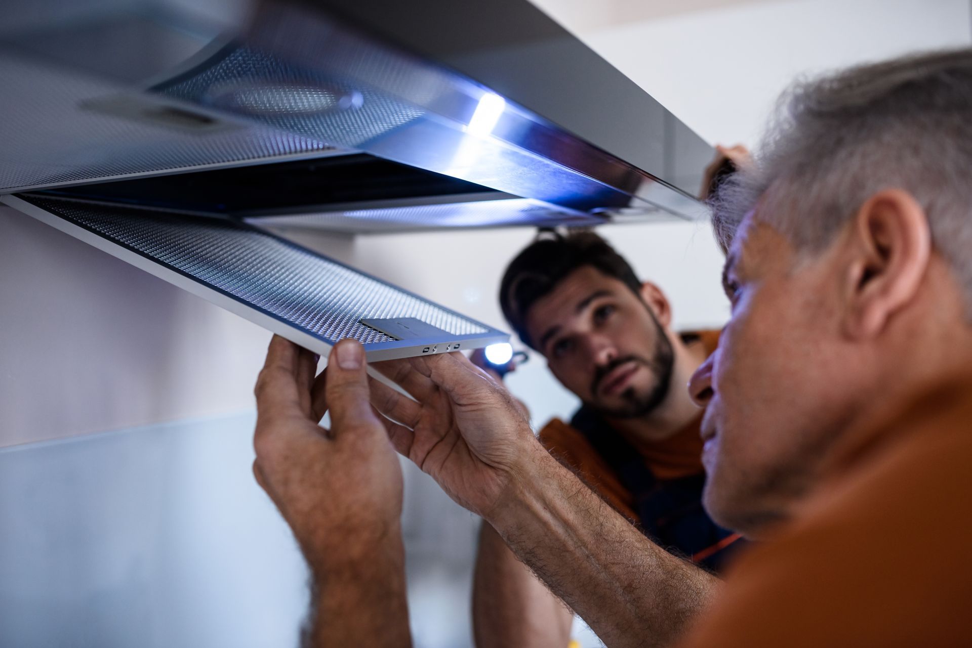 Two workers in uniform looking up at a kitchen extractor to access cleaning.