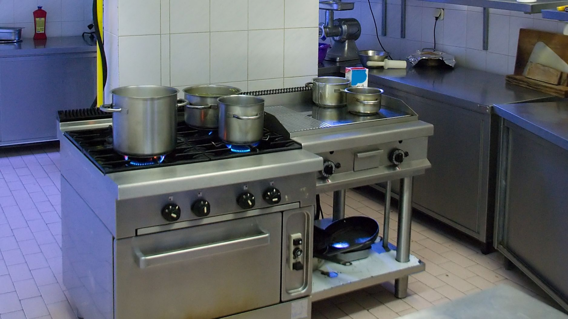 Commercial kitchen hood installation in a well-equipped kitchen with stainless steel appliances.