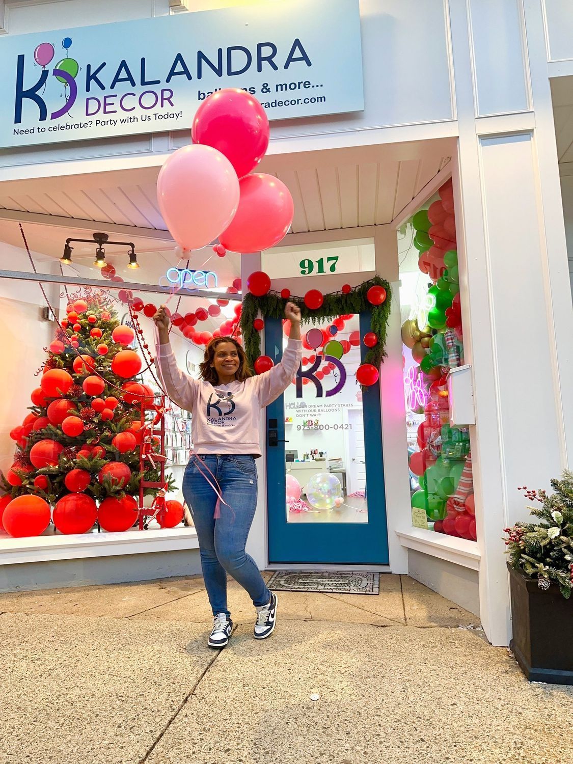 Woman holding balloons in front of a store with a Christmas display.