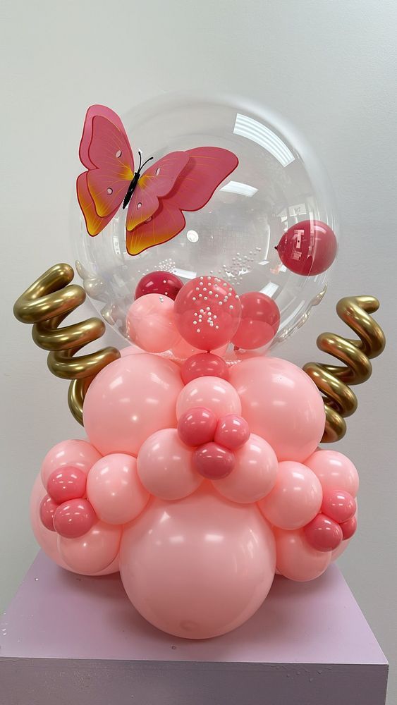 Pink and gold balloon sculpture with a butterfly inside a clear orb and heart-shaped balloons.