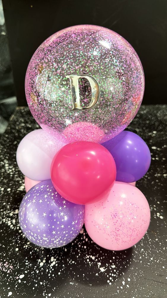 Pink and purple balloon arrangement with a glitter-filled bubble balloon topped with the letter 