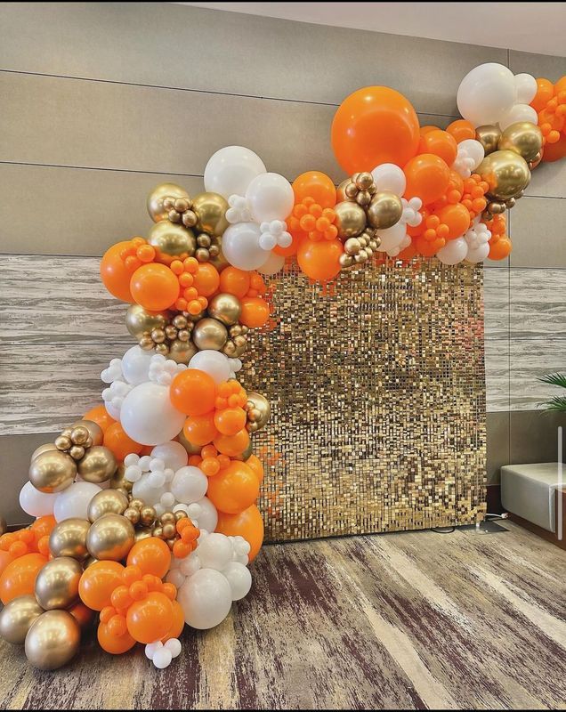 Orange, gold, and white balloon garland on a gold sequined backdrop.