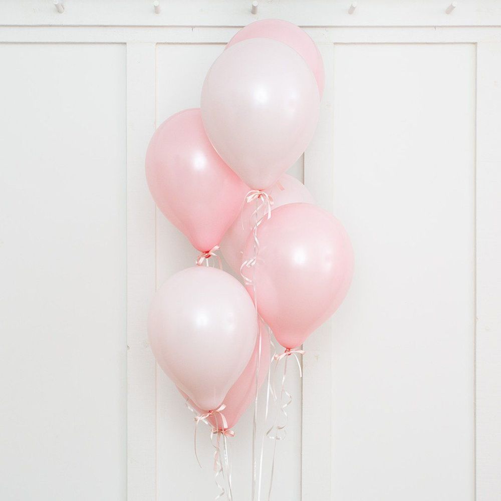 Pink and white balloons tied together, set against a white wall.