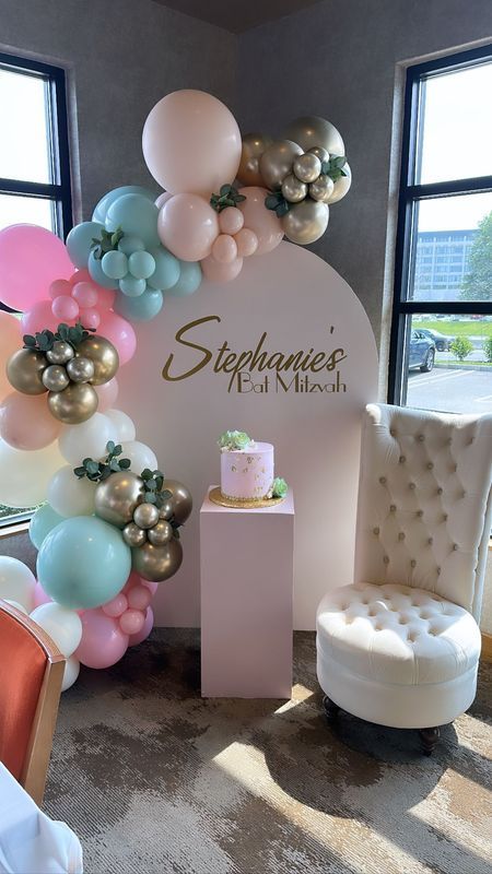 Party setup with pastel balloons, a pink cake, and a sign that reads 
