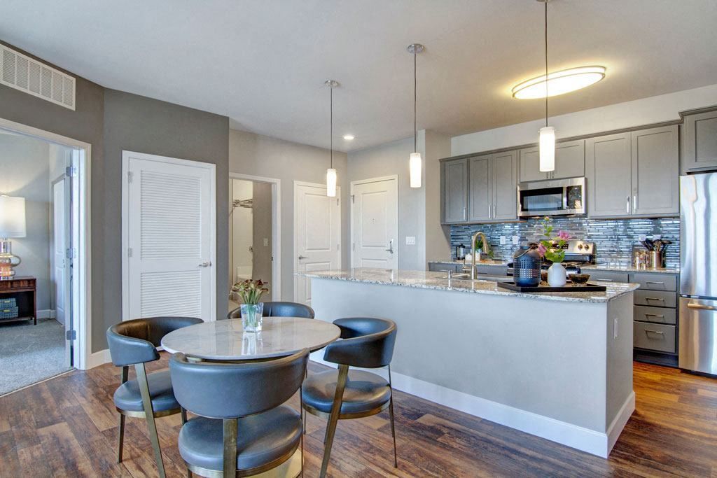 Modern kitchen with island, dining table, and stainless steel appliances. Gray and white color scheme.