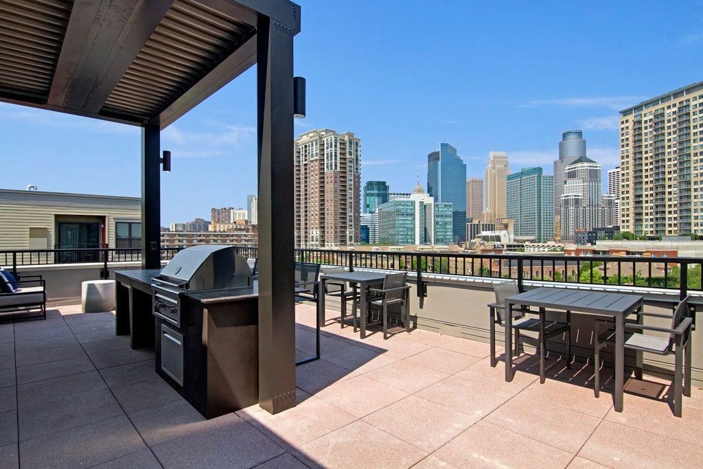 A rooftop patio with a grill and tables with a city skyline in the background