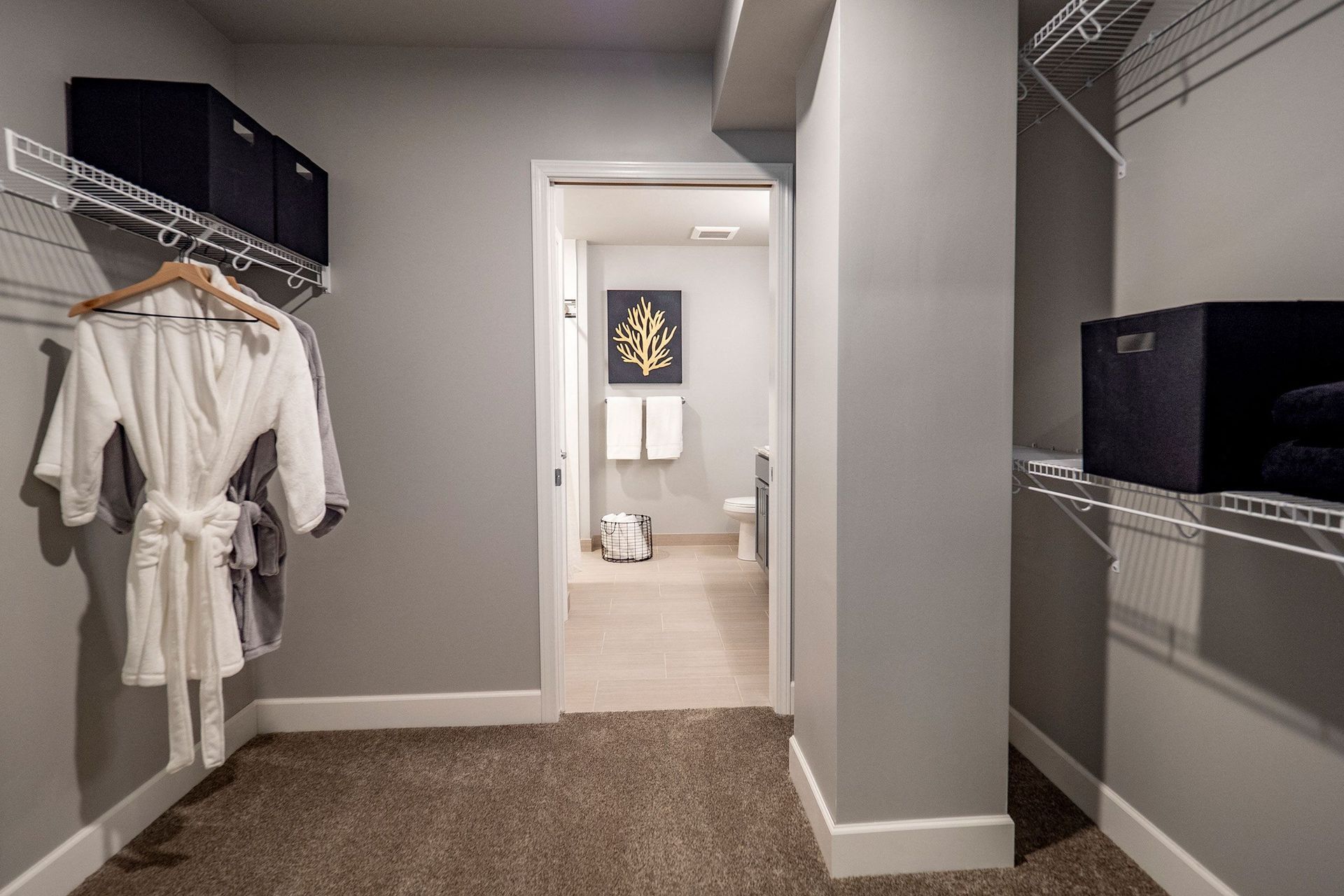 A walk in closet with a robe hanging on the wall and a bathroom in the background.