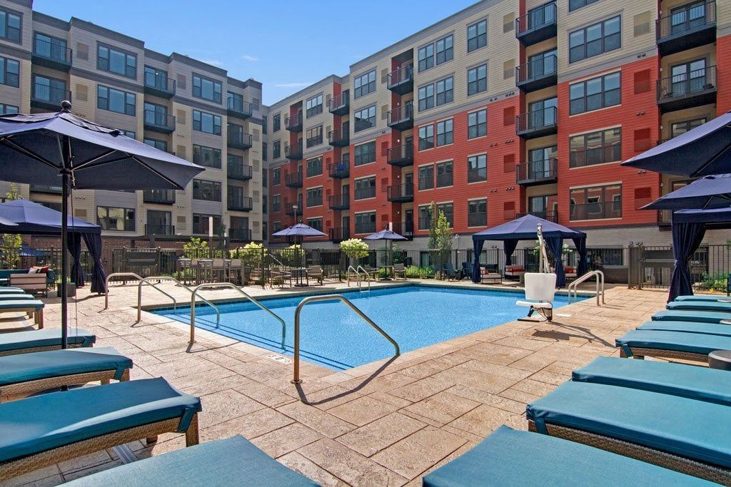 A large swimming pool surrounded by chairs and umbrellas in front of a building.