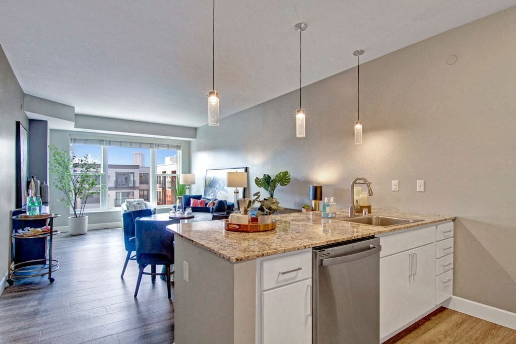 A kitchen with granite counter tops , white cabinets , a sink , and a dishwasher.