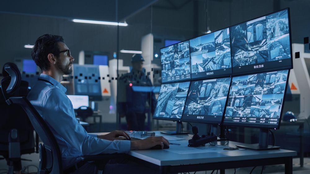 A man is sitting at a desk in front of a bunch of monitors.