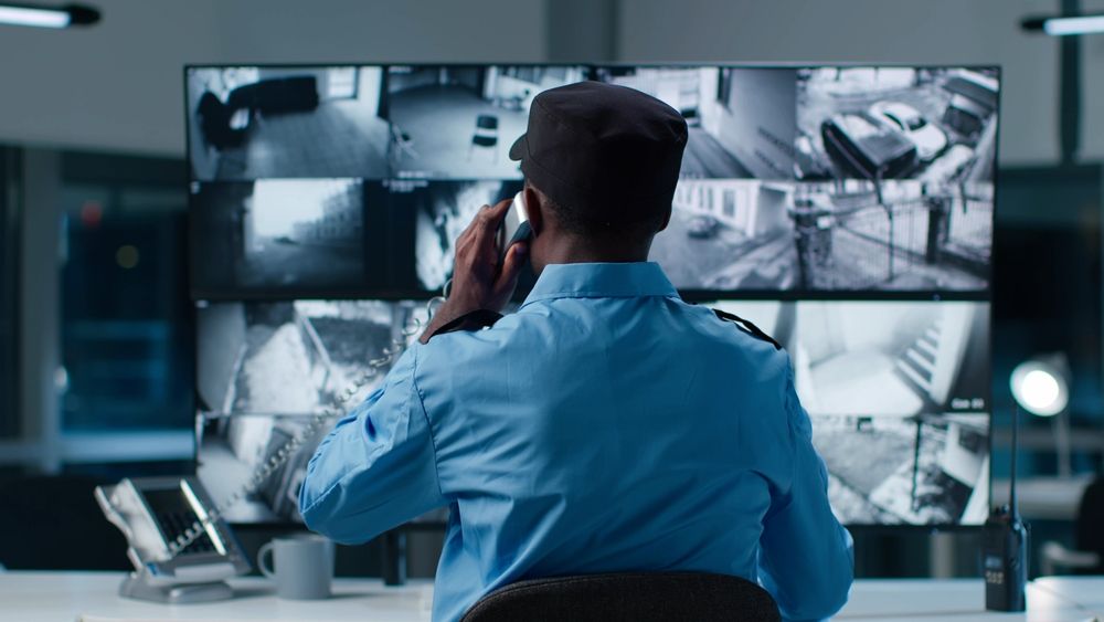 A security guard is talking on a cell phone in front of a large screen.