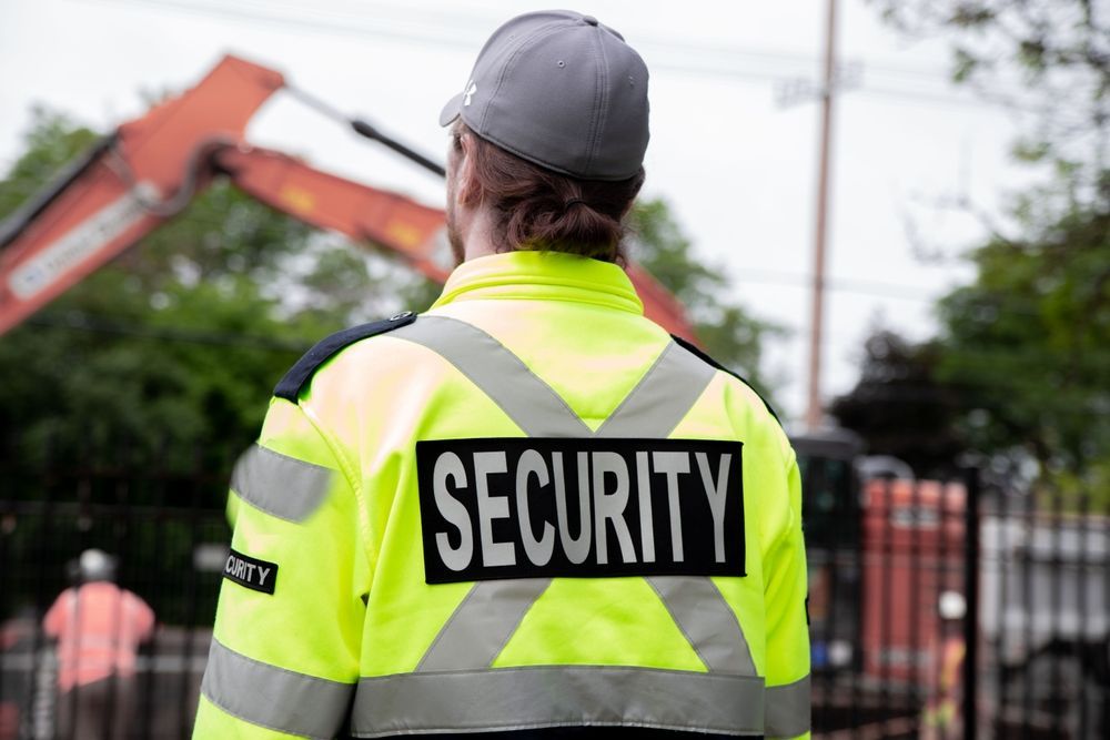 A security guard is wearing a yellow jacket with the word security on it.