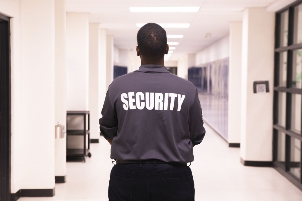 A security guard is standing in a hallway with his back to the camera