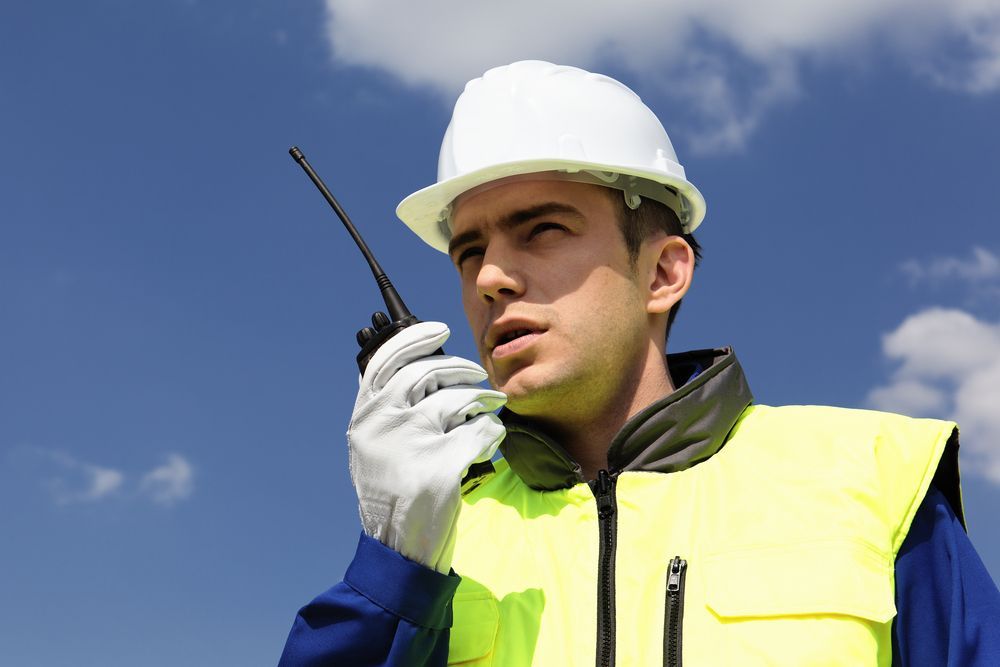 A man wearing a hard hat and safety vest is talking on a walkie talkie.