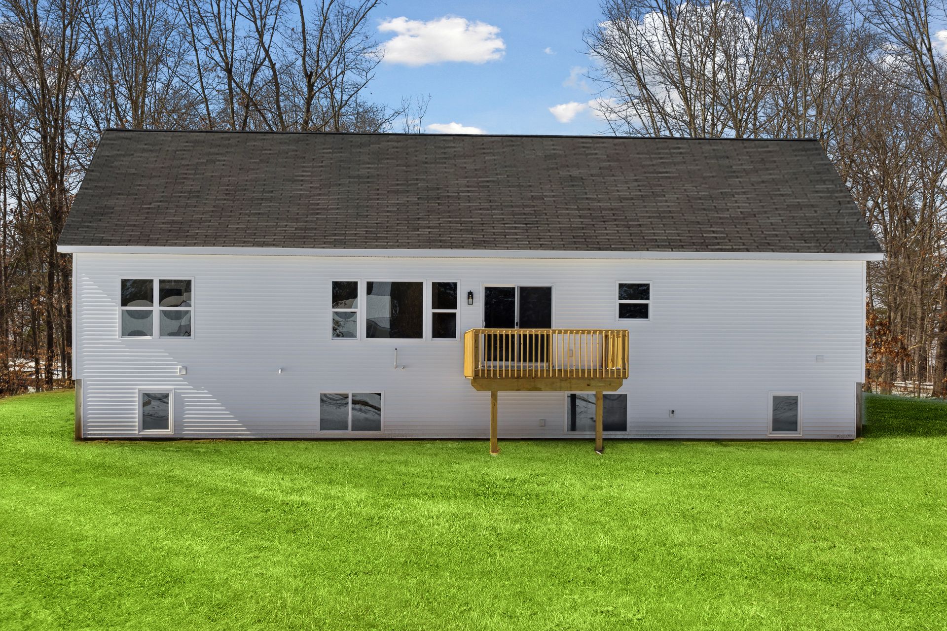 White house with a brown roof and a wooden deck, set against a green lawn and trees.
