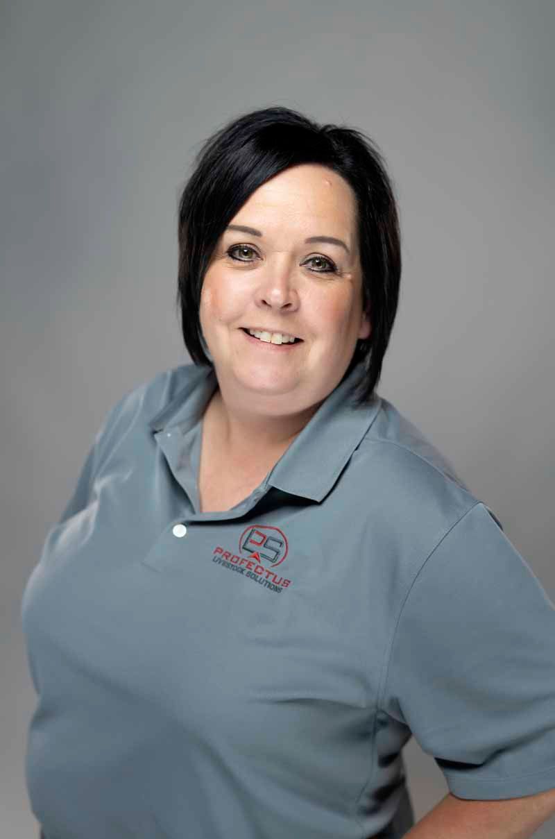 Woman with short black hair and a grey polo shirt smiles, posing for a photo against a grey background.
