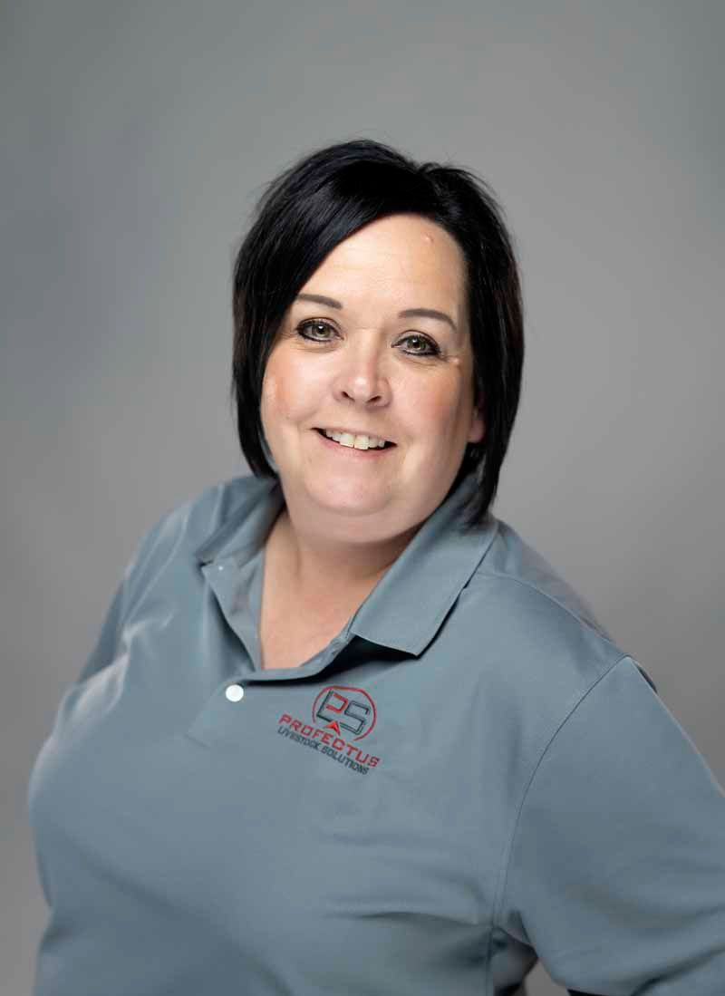 Woman with short black hair and a grey polo shirt smiles, posing for a photo against a grey background.