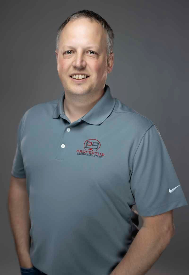 Man in a gray polo shirt smiles at the camera. The shirt has a logo and a small Nike emblem. He is against a gray backdrop.