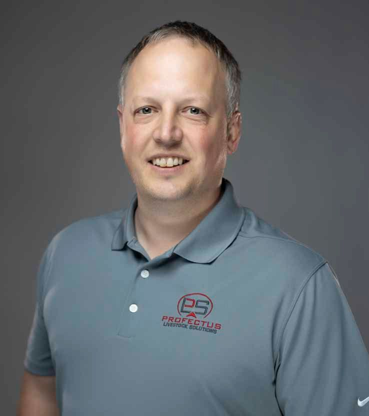 Man in a gray polo shirt smiles at the camera. The shirt has a logo and a small Nike emblem. He is against a gray backdrop.