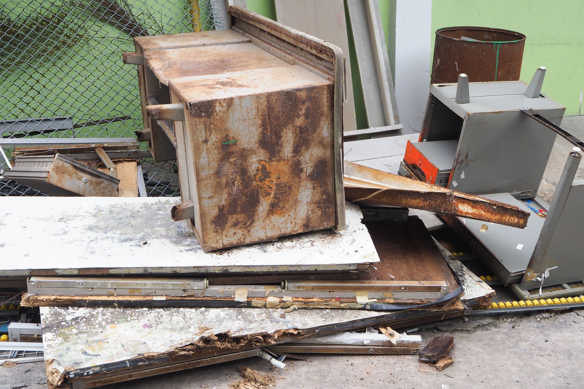 Rusty metal debris and broken boards scattered beside a chain-link fence outdoors