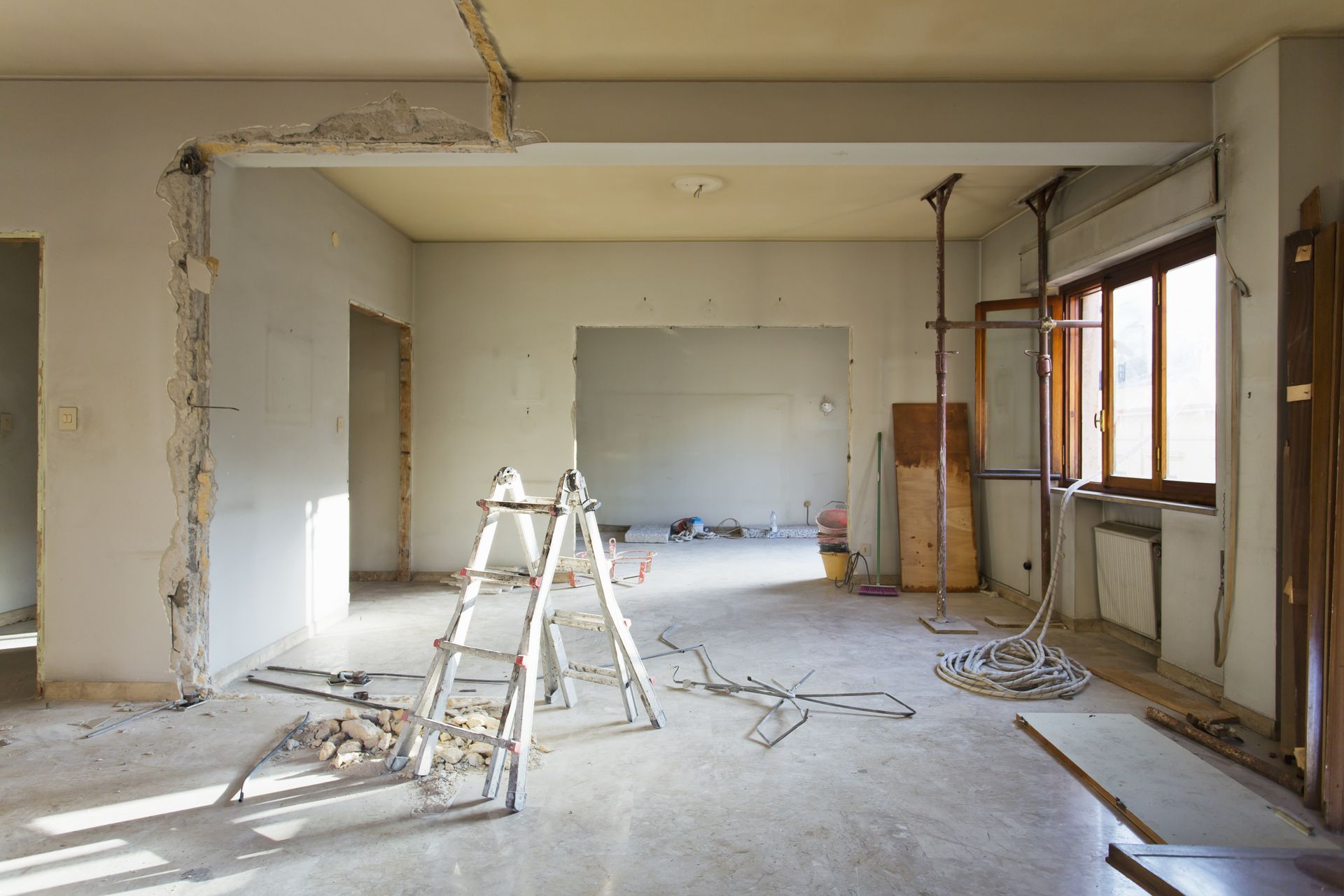 Renovation in progress in an empty room with ladders, exposed walls, and construction debris.