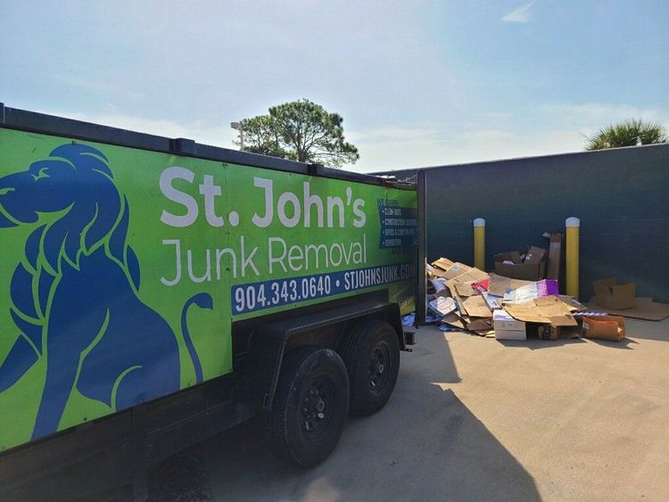 St. John's Junk Removal truck parked beside piled furniture and debris at a facility loading area