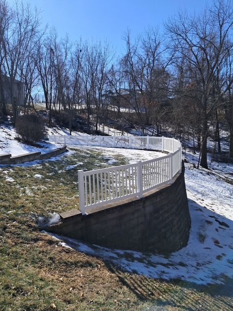 White fence on a curved retaining wall on a hillside covered with patches of snow. Blue sky in background.