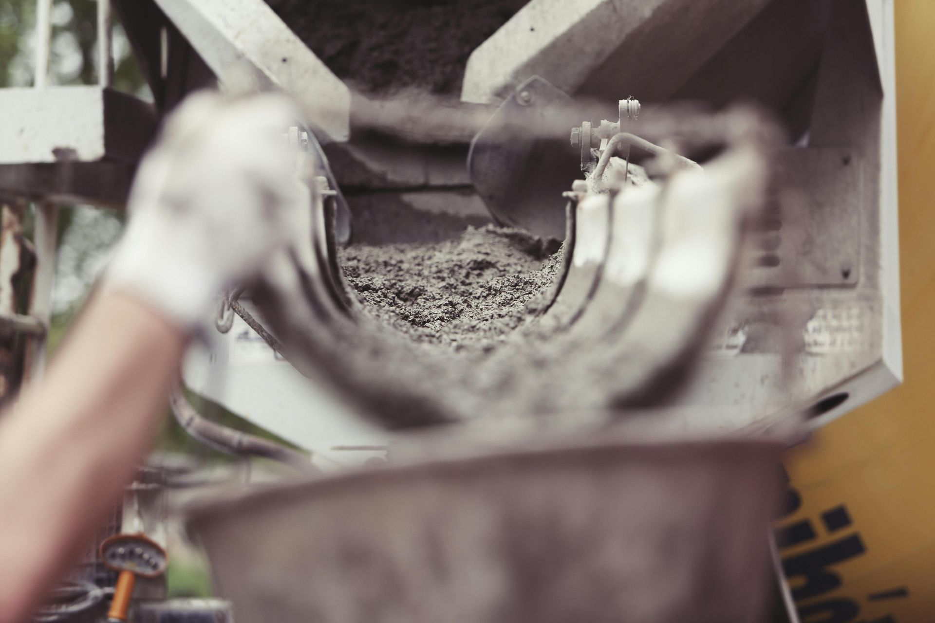 Gloved hands holding a metal ring over a concrete mixer chute with gravel inside