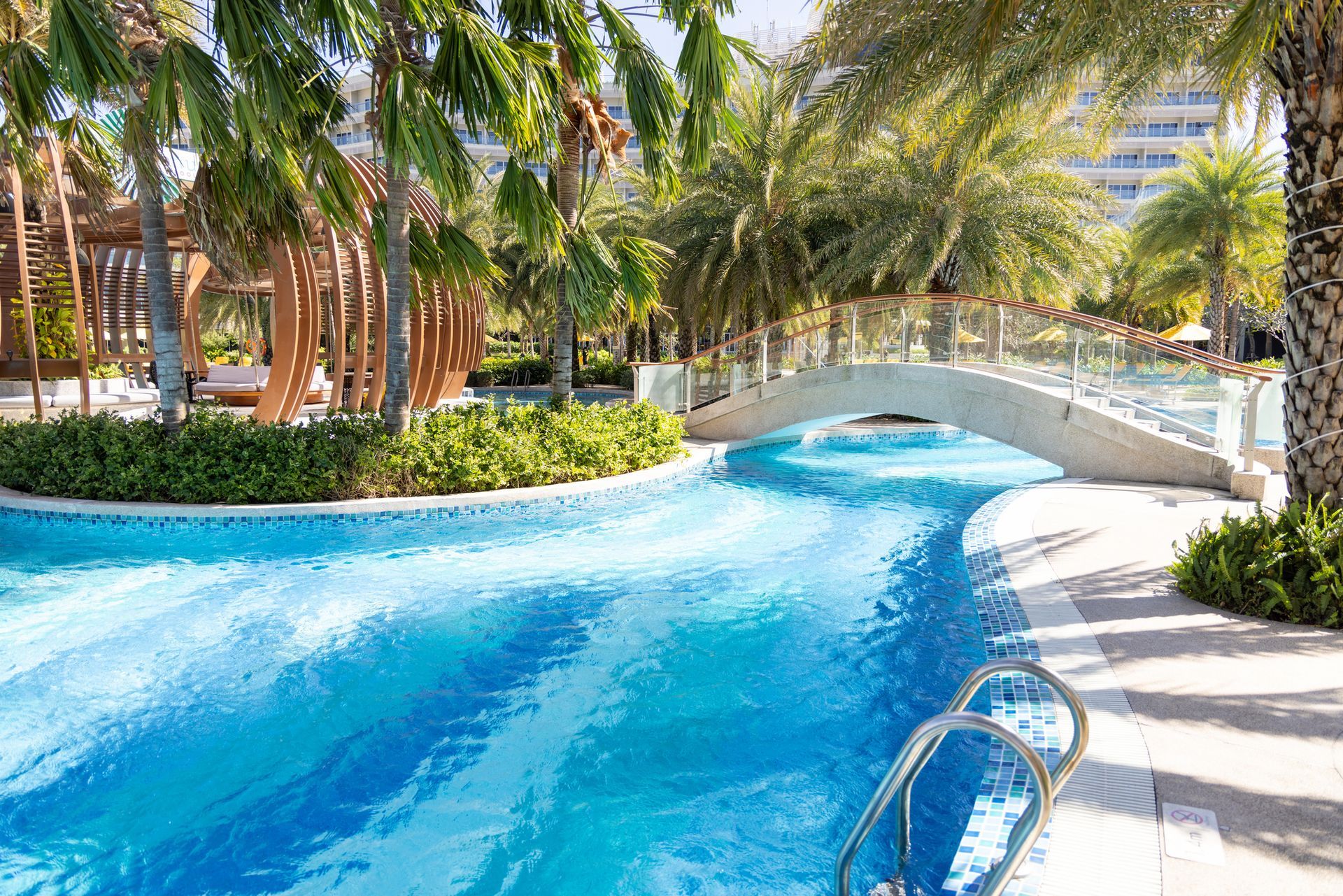 A large swimming pool surrounded by palm trees and a bridge.