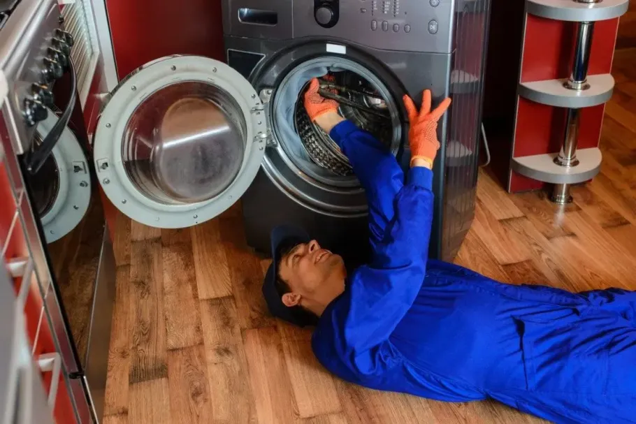 Technician in blue coveralls repairing a silver washing machine.