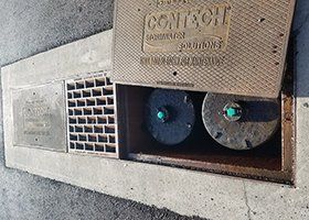 A manhole cover on the side of a road with two drains in it.